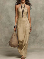 ZOFIA ATELIER beige linen blend halter neck maxi dress with a cross-front V-neckline. Model holding a woven bag.
